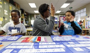 In this photo taken Wednesday, Feb. 6, 2013, Malachi Stewart, right, high-fives educational assistant Addison Hawk as Ahmed Omar continues with his work in their kindergarten classroom at Campbell Hill Elementary in Renton, Wash.  (AP Photo/Elaine Thompson)