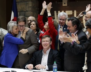 Rep. Joann Ginal, left, hugs Rep. Mark Ferrandino, after Colorado Gov. John Hickenlooper, seated center, signed the Civil Unions Act into law at the Colorado History Museum in Denver, Colo., on Thursday, March 21, 2013. (AP Photo/Brennan Linsley)
