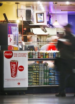 FILE - In this March 8, 2013 file photo, a Coca-Cola poster about the city's anticipated beverage ban is displayed at a pizza shop at New York's Penn Station.  New York City's groundbreaking limit on the size of sugar-laden drinks has been struck down by a judge shortly before it was set to take effect. The restriction was supposed to start Tuesday, March 12, 2013. The rule prohibits selling non-diet soda and some other sugary beverages in containers bigger than 16 ounces. It applies at places ranging from pizzerias to sports stadiums, though not at supermarkets or convenience stores.  (AP Photo/Bebeto Matthews)