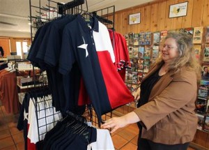 Tourism manager Susan Morton points out some top-selling items at Waco’s Tourist Information Center, such as this Texas flag-themed polo shirt. Morton said postcards and collectibles such as spoons also are popular. (Waco Tribune-Herald)