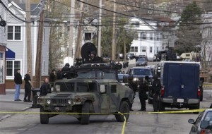Officials wearing tactical gear stand near an armored vehicle as they search an apartment building for one of two suspects in the Boston Marathon bombing, in Watertown, Mass., Friday, April 19, 2013. Two suspects in the Boston Marathon bombing killed an MIT police officer, injured a transit officer in a firefight and threw explosive devices at police during a getaway attempt in a long night of violence that left one of them dead and another still at large Friday, authorities said as the manhunt intensified for a young man described as a dangerous terrorist. (AP Photo/Julio Cortez)
