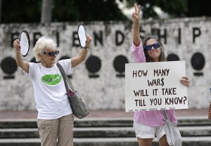 Sigrud Ofengand, left, and Barbara Green, wave to passing cars during a rally opposing the possibility of U.S. military intervention in Syria on Monday, Sept. 9, 2013, in Miami. President Barack Obama has called on Congress to approve the use of military force in the wake of a deadly chemical weapons attack his administration blames on the Syrian government. (AP Photo/Wilfredo Lee)