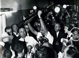 Ed DeLong, former Lariat associate editor, reports at the Dallas Police Station on Nov. 22, 1963, as police officers parade through the hall with the rifle thought to be used by Oswald to kill the president.  (Courtesy Photo)