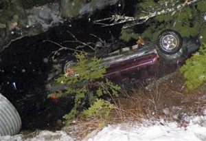 The SUV from which the infant was rescued rests upside down in water alongside Route 6 Monday in Kossuth Township, Maine.Associated Press