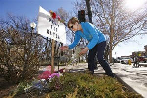 In this photo taken on Monday, Feb. 9, 2015, Turi Whiting of Minneapolis leaves a bouquet of flowers at a "Pray for Kayla" sign in downtown Prescott, Ariz. Mueller, a 26-year-old American woman held by Islamic State militants, has been confirmed dead, her parents and the Obama administration said Tuesday, Feb. 10, 2015. The White House said that Mueller's family received a private message from her captors over the weekend and the information contained in that communication was authenticated by the U.S. intelligence community. It was not immediately clear how and when Mueller died. (AP Photo/The Arizona Republic, Rob Schumacher )  
