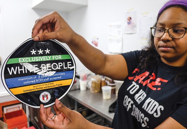 April Jensen, an employee at Sugar Mama's holds a sticker that the business found Wednesday on the front of their store in Austin.  Associated Press