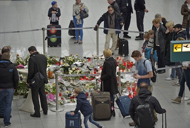 Passengers watch candles and flowers for the victims of the plane crash Tuesday at the airport in Dusseldorf , Germany. One week ago 150 people died in the Germanwings airliner crash in the French alps on its way from Barcelona to Duesseldorf.  Associated Press
