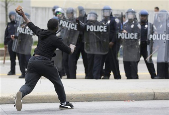 A man throws a brick at police Monday following the funeral of Freddie Gray, an African-American who died of a spine injury while in police custody, in Baltimore. A curfew has been put in place amid riots.  Associated Press