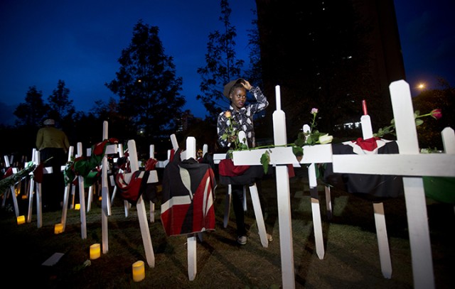 A Kenyan woman holding a rose removes her hat Tuesday as she lights candles next to a white wooden cross for each of the victims of the Garissa attack, during a vigil at Uhuru Park in Nairobi, Kenya. Associated Press