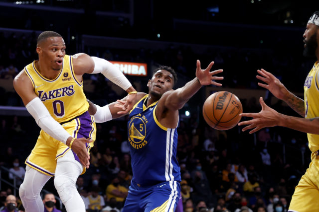 Los Angeles Lakers guard Russell Westbrook, left, passes the ball to forward Anthony Davis, right, while defended by Golden State Warriors center Kevon Looney during the first half of a preseason NBA basketball game in Los Angeles, Tuesday, Oct. 12, 2021. (AP Photo/Ringo H.W. Chiu)