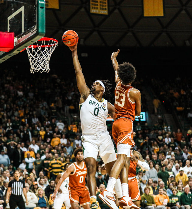 Fifth-year senior forward Flo Thamba (0) leaps by a defender and tries to dunk the ball during a conference game against No. 8 University of Texas, Saturday, Feb. 25, 2023, in the Ferrell Center.Kenneth Prabhakar | Photo Editor