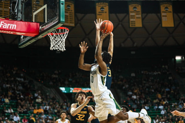 Redshirt senior guard Adam Flagler (10) releases a tough layup layup attempt with a Mountaineer contesting it during a conference game against West Virginia University, on Feb. 13, 2023, in the Ferrell Center.Kenneth Prabhakar | Photo Editor