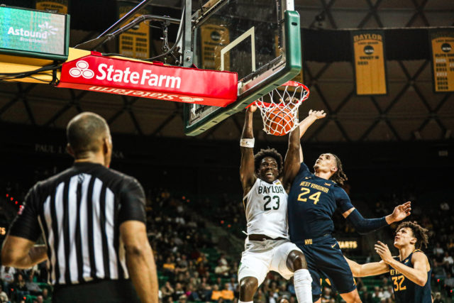 Redshirt senior forward Jonathan Tchamwa Tchatchoua (23) slams down a dunk over a Mountaineer defender during a conference game against West Virginia University, on Feb. 13, 2023, in the Ferrell Center.Kenneth Prabhakar | Photo Editor