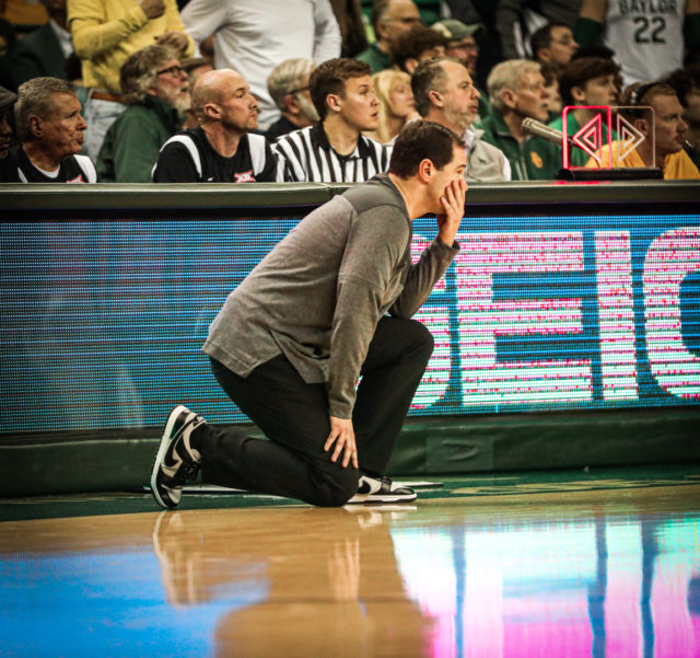 Head coach Scott Drew kneels near midcourt on the sideline as he watches the play unfold during a conference game against West Virginia University, on Feb. 13, 2023, in the Ferrell Center.Kenneth Prabhakar | Photo Editor