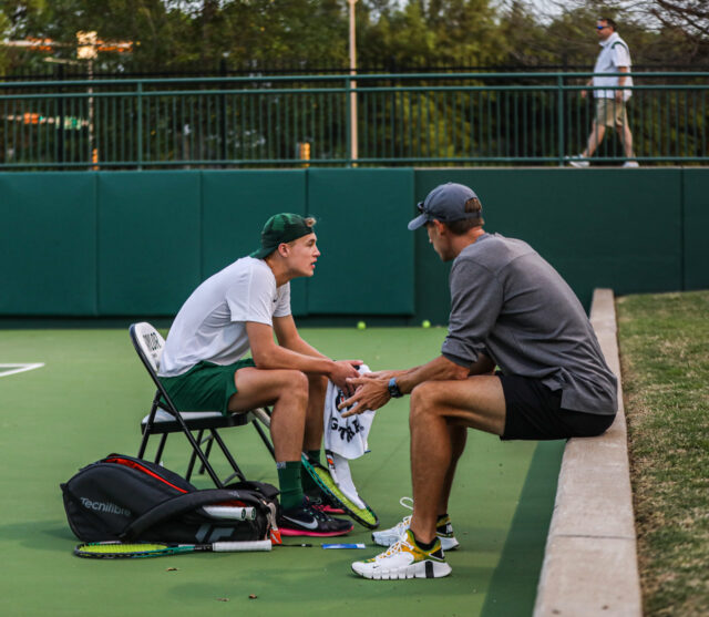 Head coach Michael Woodson (right) sits and chats with freshman Luc Koenig (left) in between action during Baylor men's tennis' Saturday doubleheader against the University of Texas Rio Grande Valley and Texas Tech University on April 1 at the Hurd Tennis Center. Kenneth Prabhakar | Photo Editor