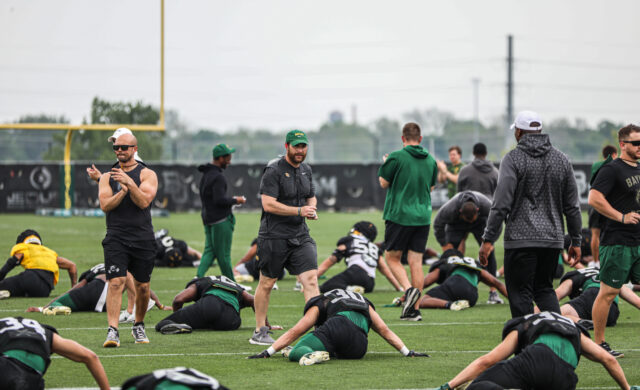 New defensive coordinator and safeties coach Matt Powledge (middle, green hat) walks through the team's stretching excercise during Baylor football's sixth day of spring practice on Tuesday at the squad's outdoor football practice field. 
Kenneth Prabhakar | Photo Editor