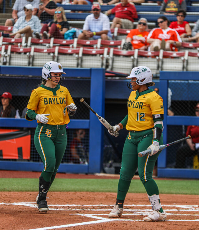 Junior utility Emily Hott (left, 4) receives her bat from sophomore first baseman Shaylon Govan (12) on her way back to the dugout during No. 4 seed Baylor softball's first round game against No. 5 seed Iowa State University as part of the Phillips 66 Big 12 Softball Championship on Thursday at USA Softball Hall of Fame Stadium in Oklahoma City.
Michael Haag | Sports Editor