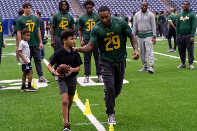 Junior Running Back Richard Reese guides children from DePelchin Children’s Center through football drills during the Kinder’s Texas Bowl DePelchin Field Day on Monday at NRG Stadium in Houston.Mesha Mittanasala| Photographer