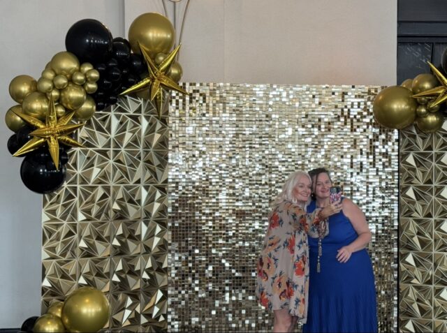 Attendees pose for a photo in front of the gold backdrop during Mission Waco’s Fashion with a Passion show at Hotel 1928.