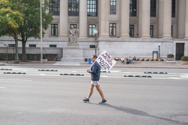 A lone protestor walks the streets of Pennsylvania Avenue carrying a sign as he makes his way towards the "No Kings" protest. Jake Schroeder | Photographer