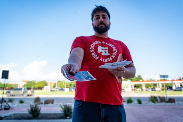 Party for Socialism and Liberation volunteer David Traverso hands out fliers during the protest across from campus Wednesday. Sam Gassaway | Photo Editor