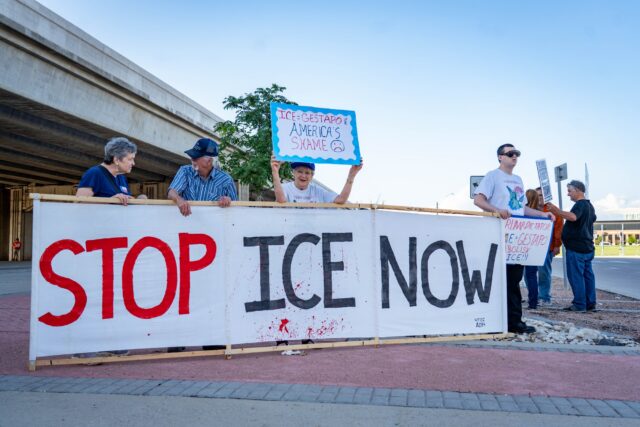 Protestors hold up a "Stop Ice Now" banner at the corner of fifth street and Jack Kultgen expressway during the protest across from campus Wednesday. Sam Gassaway | Photo Editor